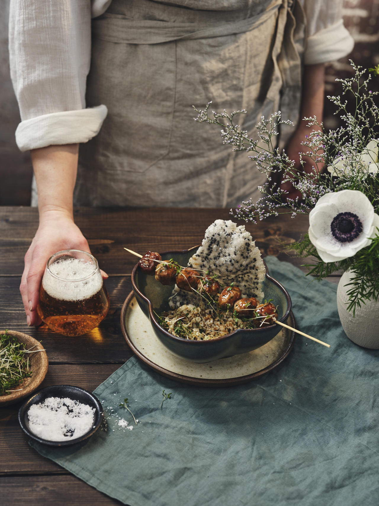 Servitören serverar ett glas öl till den japanska rätten "Niku Dango" som ligger på träbordet som är dekorerat med blommor